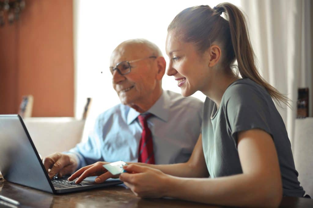 Pflegekraft sitzt mit Senior am Laptop